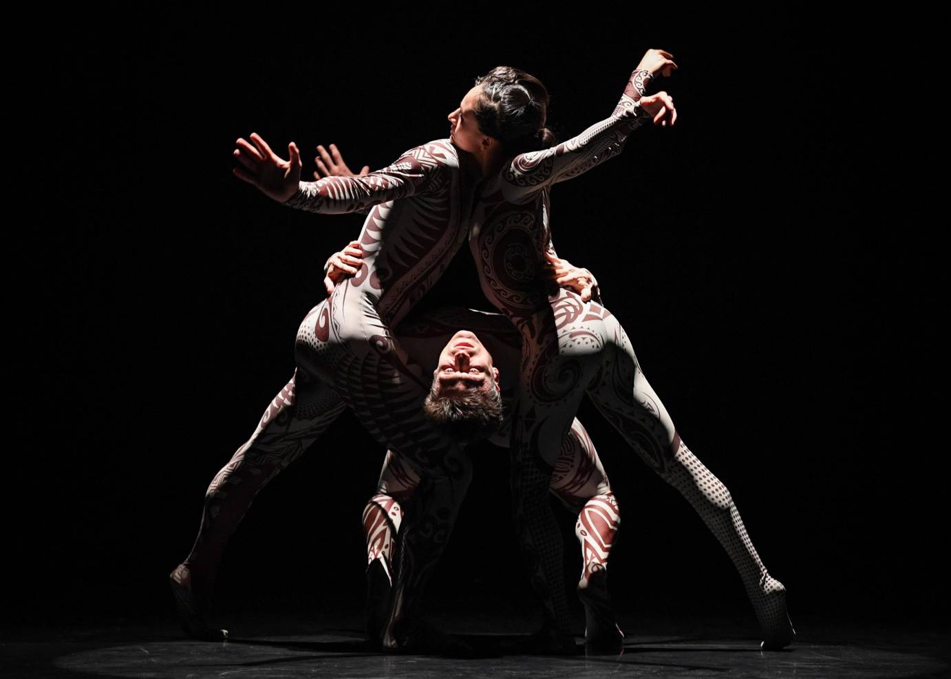 Three dancers form a triangle with their chests